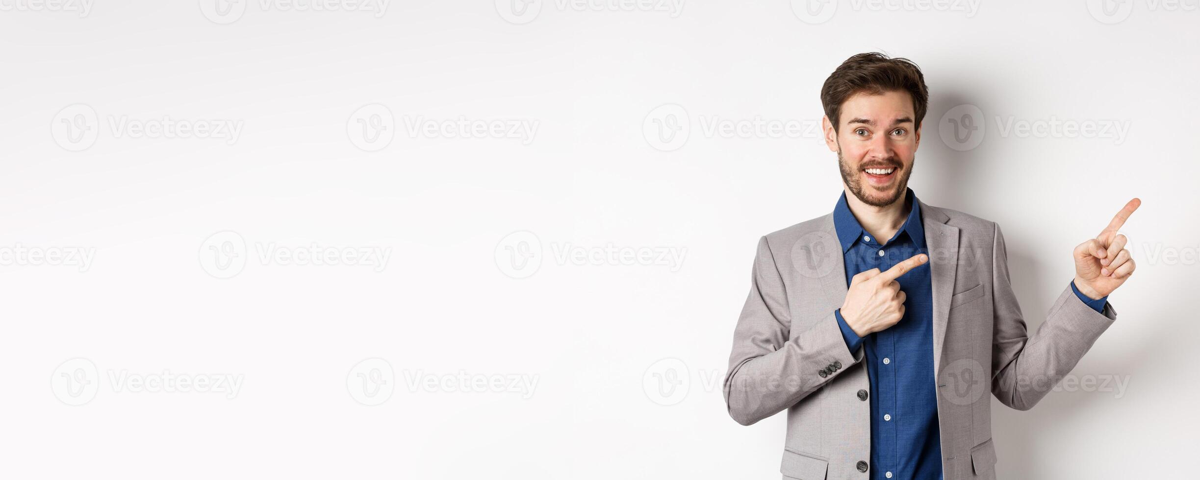 Happy businessman in suit pointing fingers right and smiling excited, showing special deal, standing on white background photo