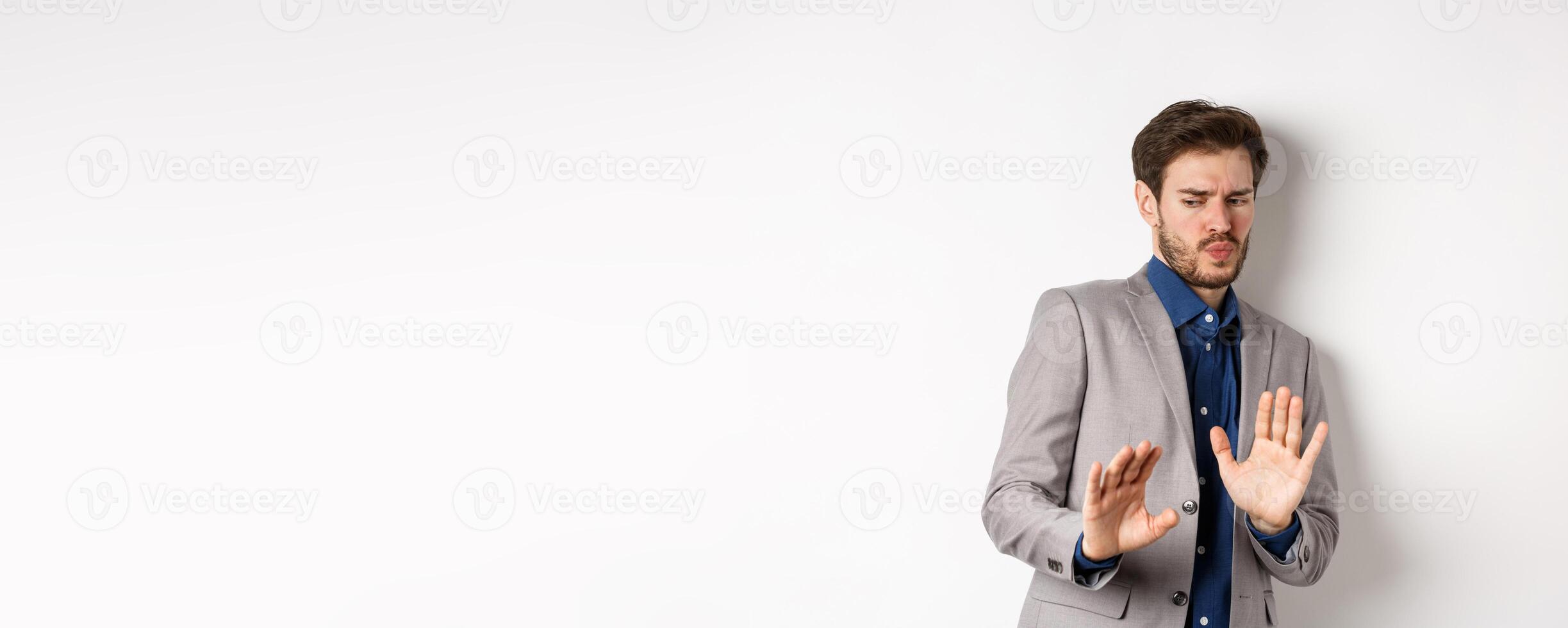 Stay away. Reluctant businessman step back with concerned disgusted face, raising hands to block bad offer, rejecting something awful, tilting from disgust, white background photo