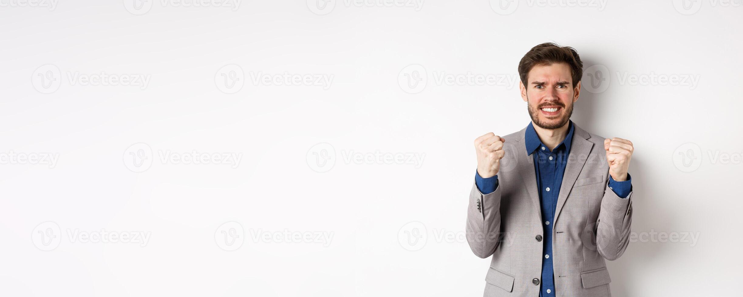 Tensed businessman feeling nervous and pressured, clenching fists and teeth, staring at camera, making money and looking worried, standing on white background photo