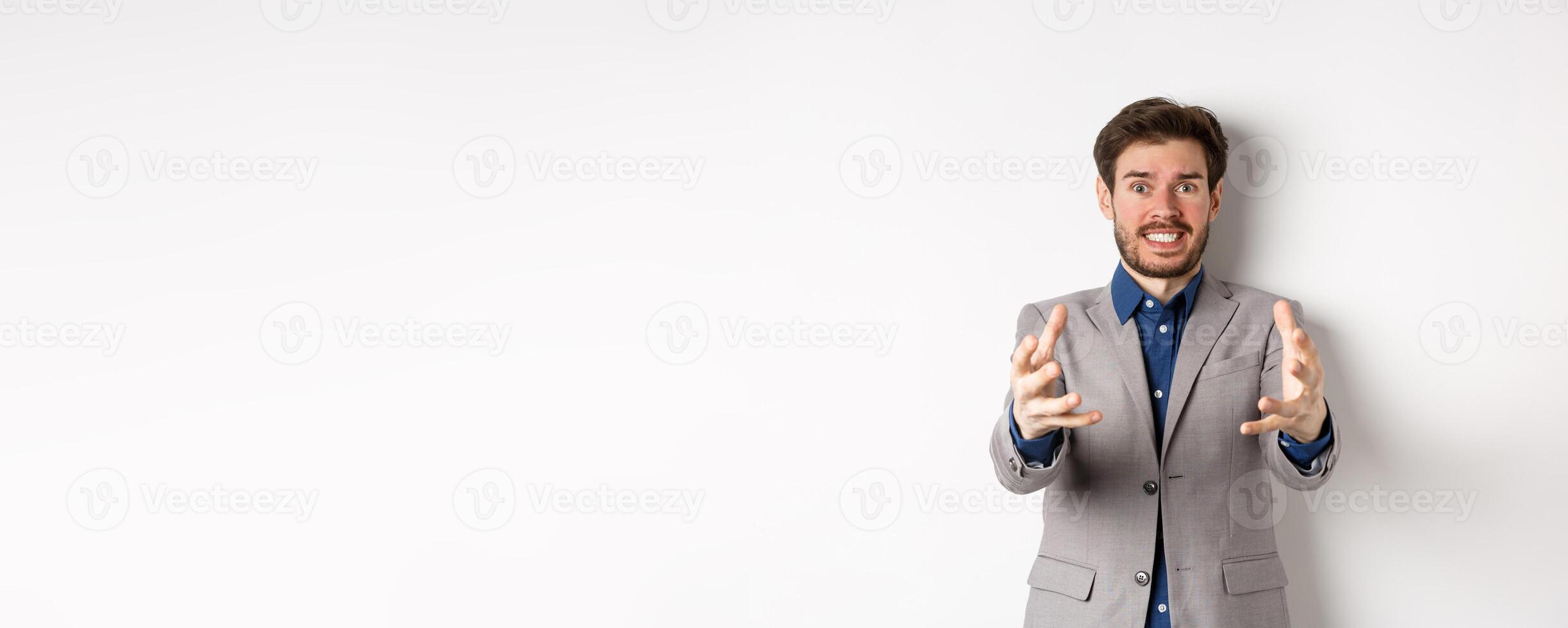 Distressed businessman stretch out hands to strangle annoying person, standing annoyed and frustrated against white background, wearing suit photo
