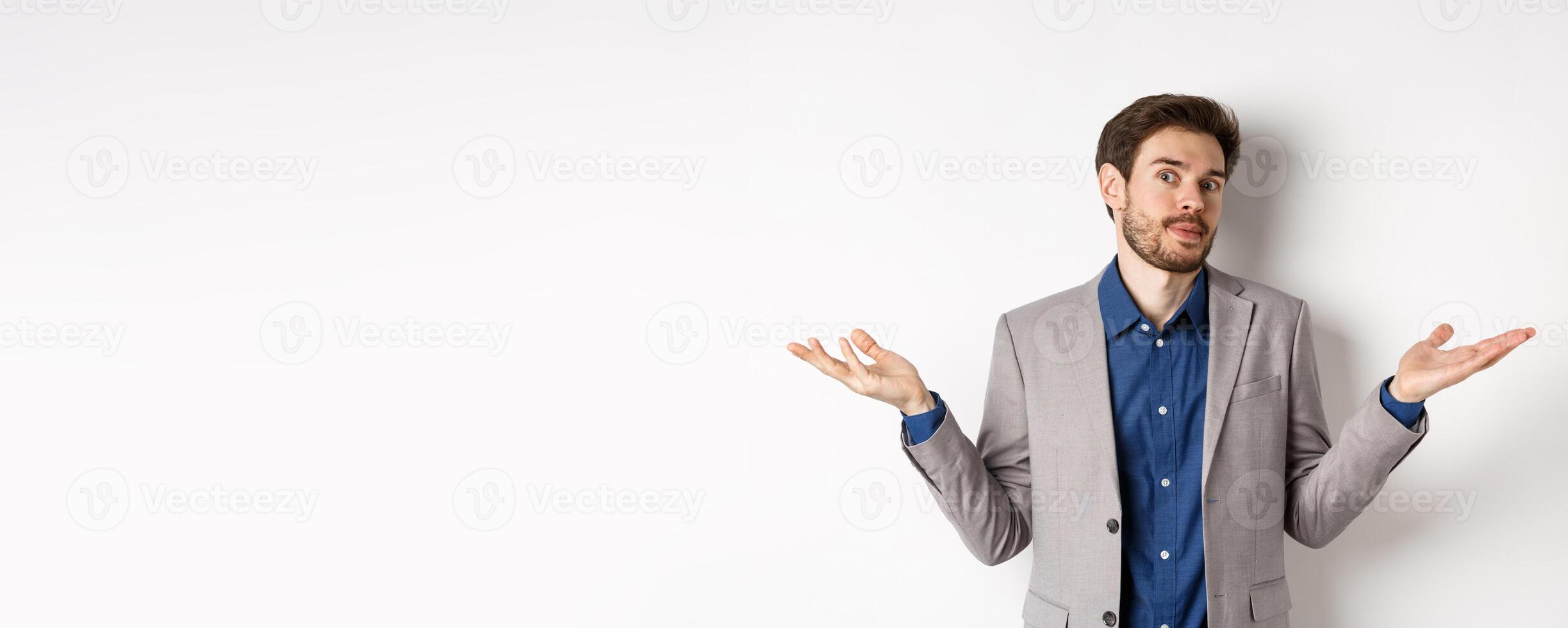 I dont know. Clueless bussiness man in suit shrugging shoulders and looking unaware, have no idea, standing on white background photo