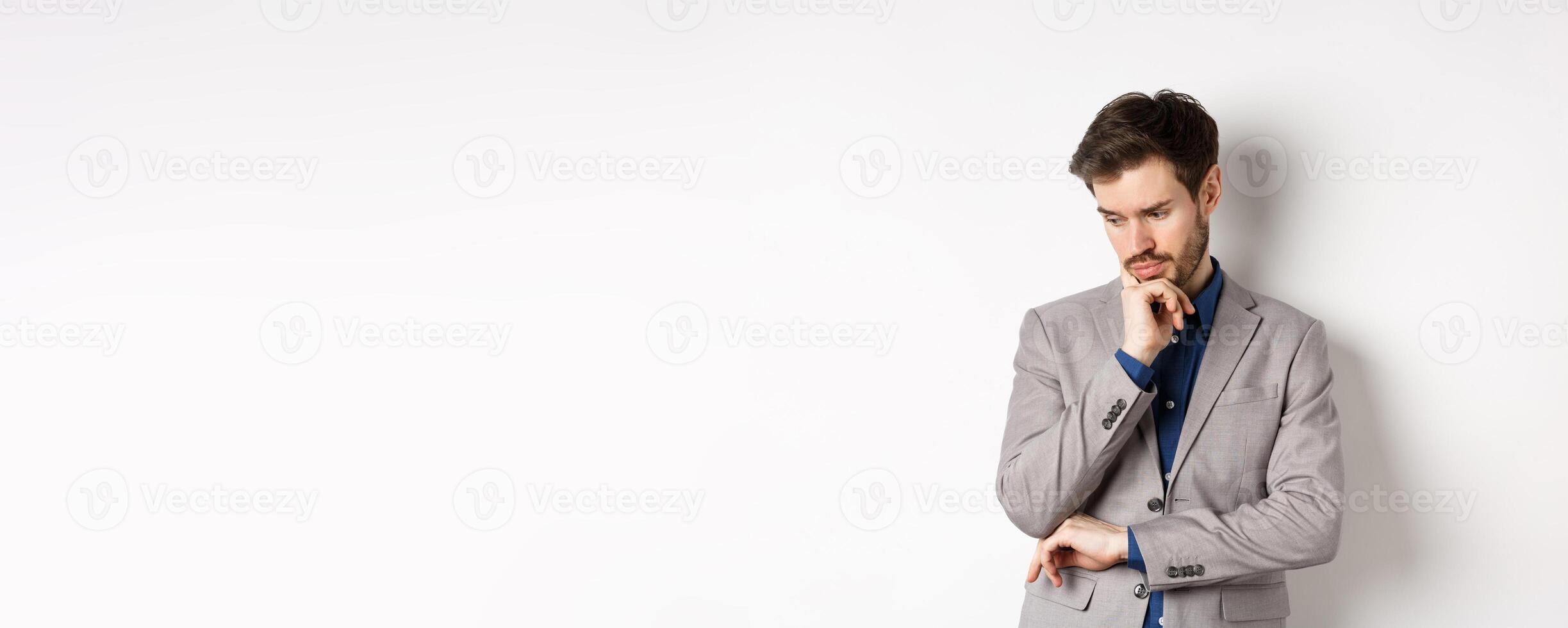 Thoughtful businessman in suit looking down and thinking, making decision, standing on white background photo