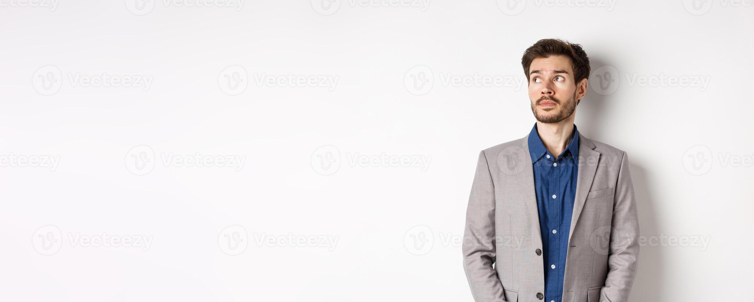 Thoughtful sad businessman in suit looking at upper left corner logo, thinking or spacing out, standing on white background photo