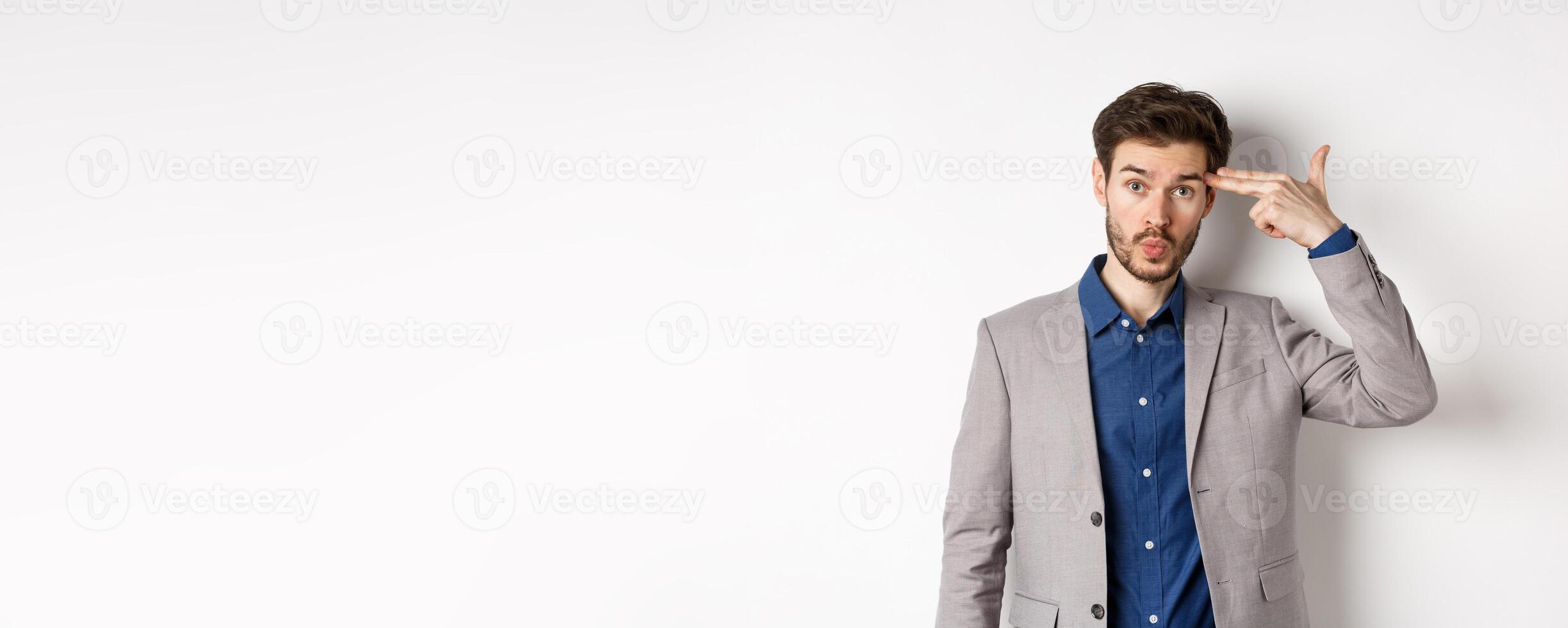 Annoyed guy in business suit shoot himself with hand gun near head, look distressed and tired after work, standing on white background photo
