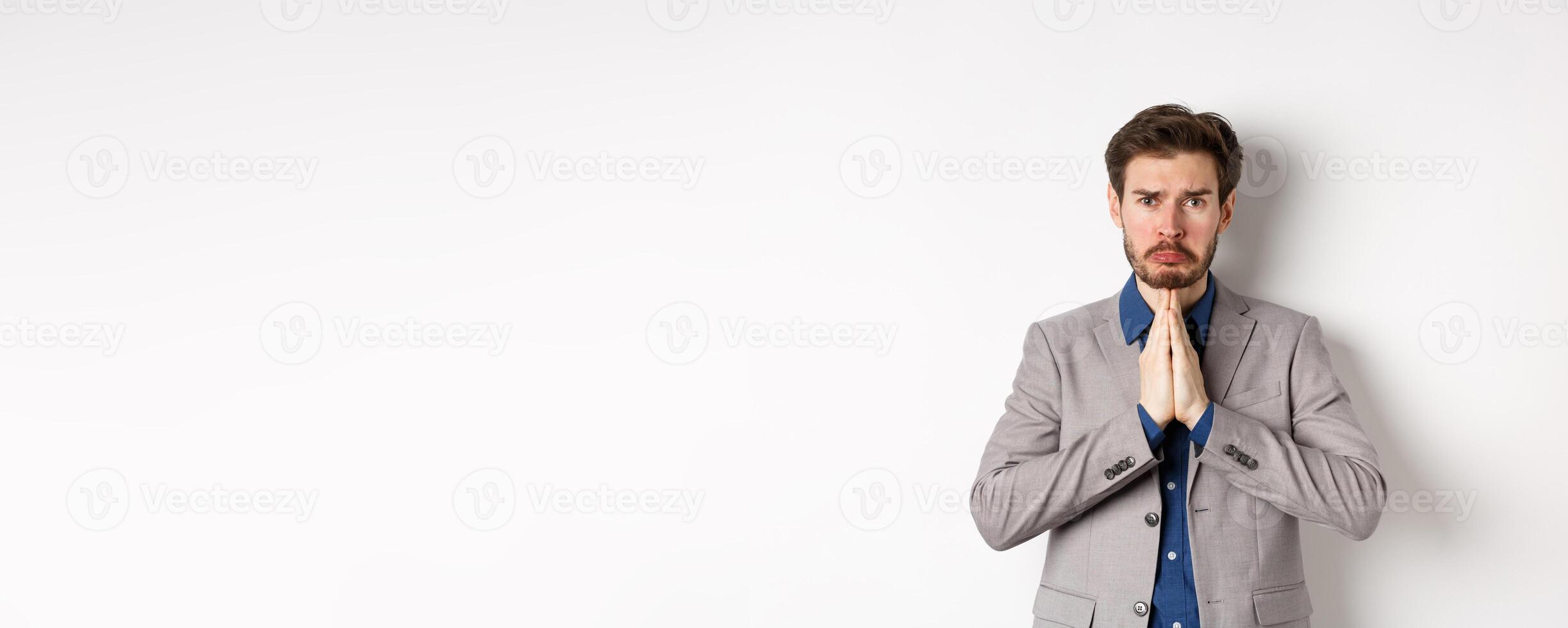 Miserable whining businessman asking for loan, need help and begging you, sobbing and say please with sad face, standing on white background, ask for forgiveness photo