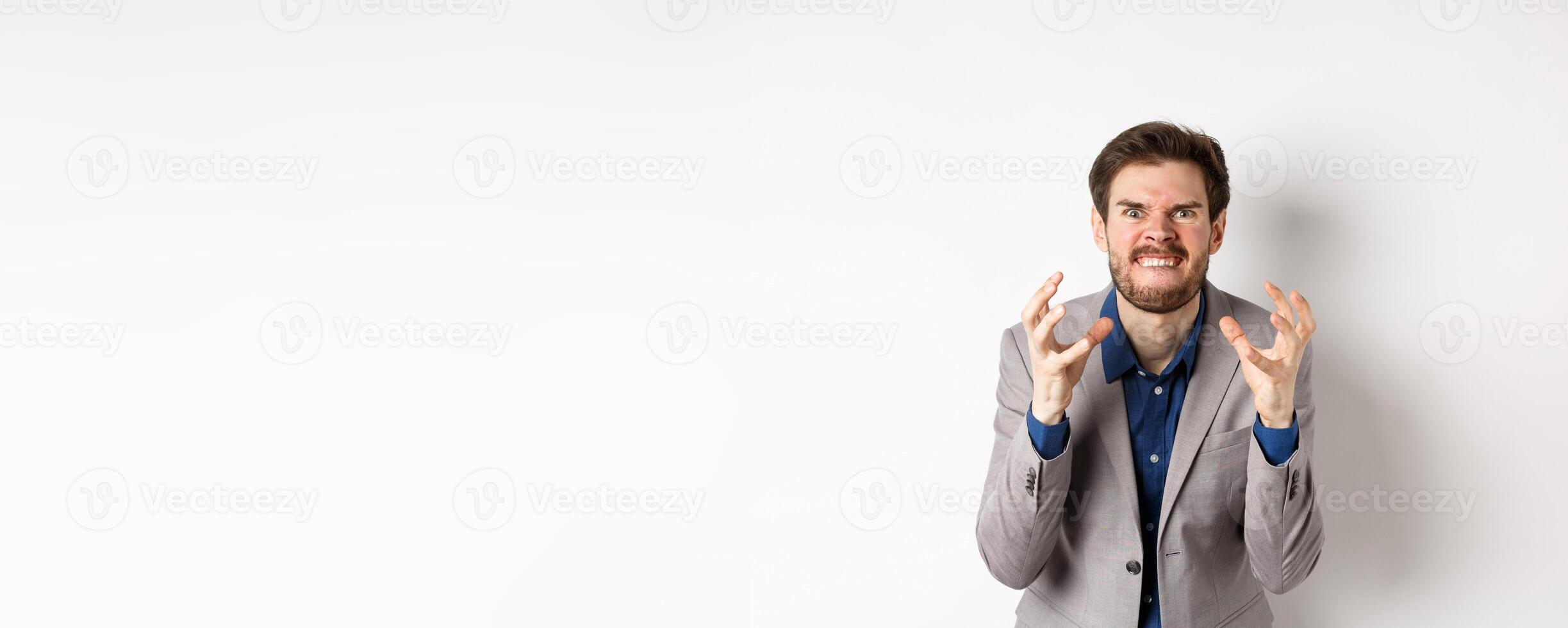 Angry and tensed businessman wants to kill someone, clenching hands and teeth, looking mad at camera, going to strangle person, standing on white background photo