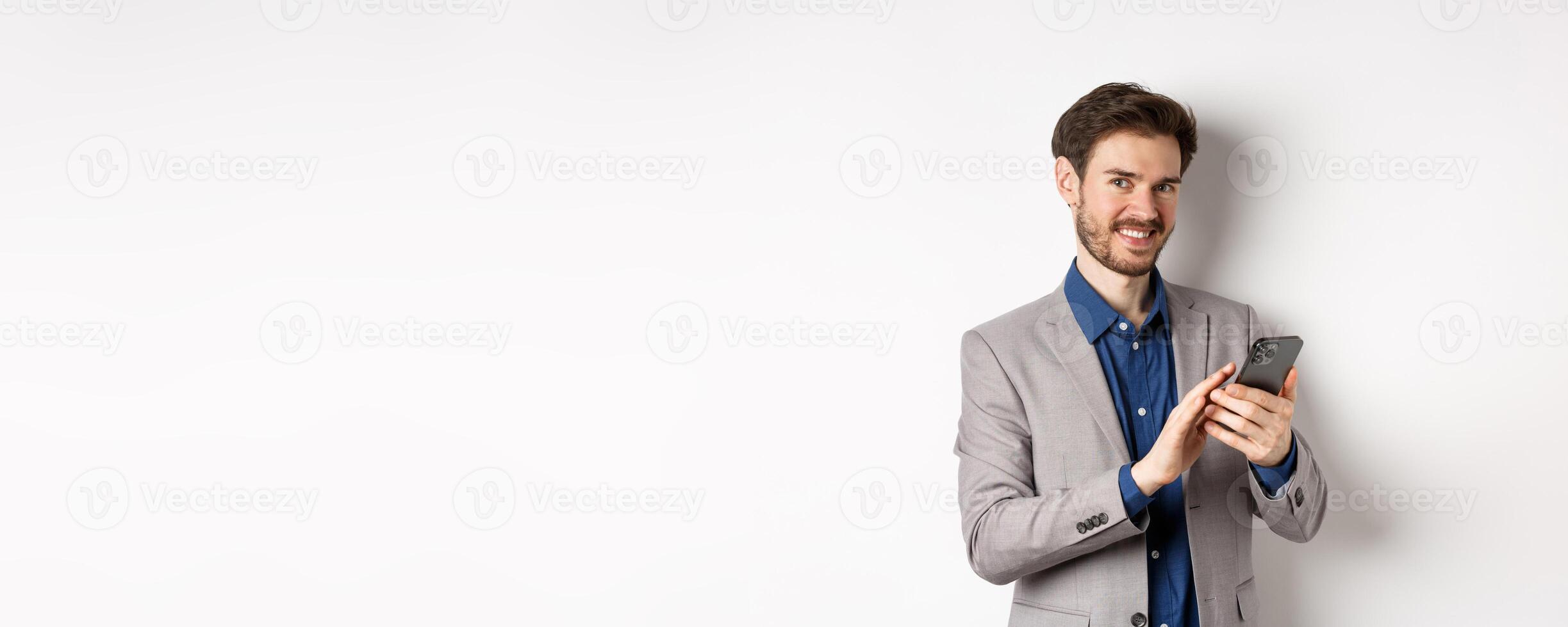 Smiling successful business man using smartphone on white background, standing in suit photo