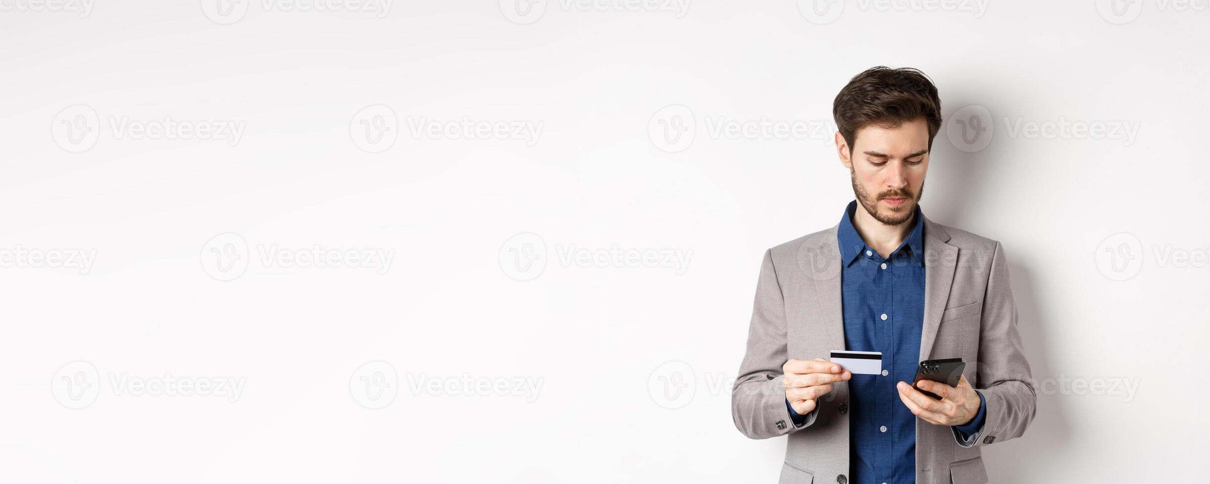 Handsome businessman paying online with credit card and smartphone, standing on white background in suit photo
