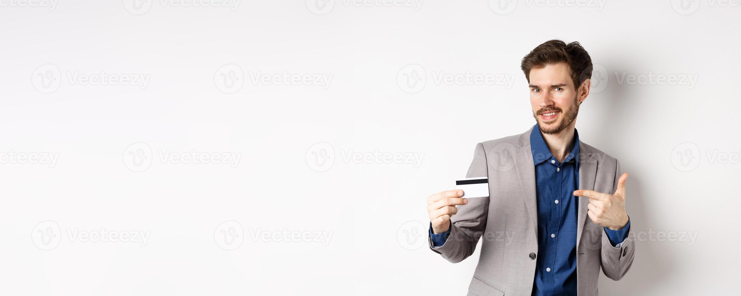 Successful male entrepreneur pointing at plastic credit card and smiling, recommending bank, standing on white background photo
