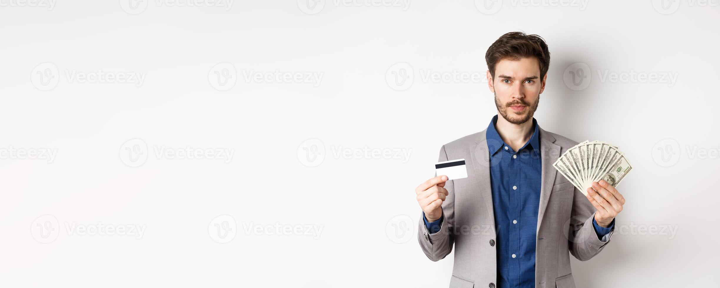 Successful businessman making money, standing in suit with dollar bills and plastic credit card, white background photo