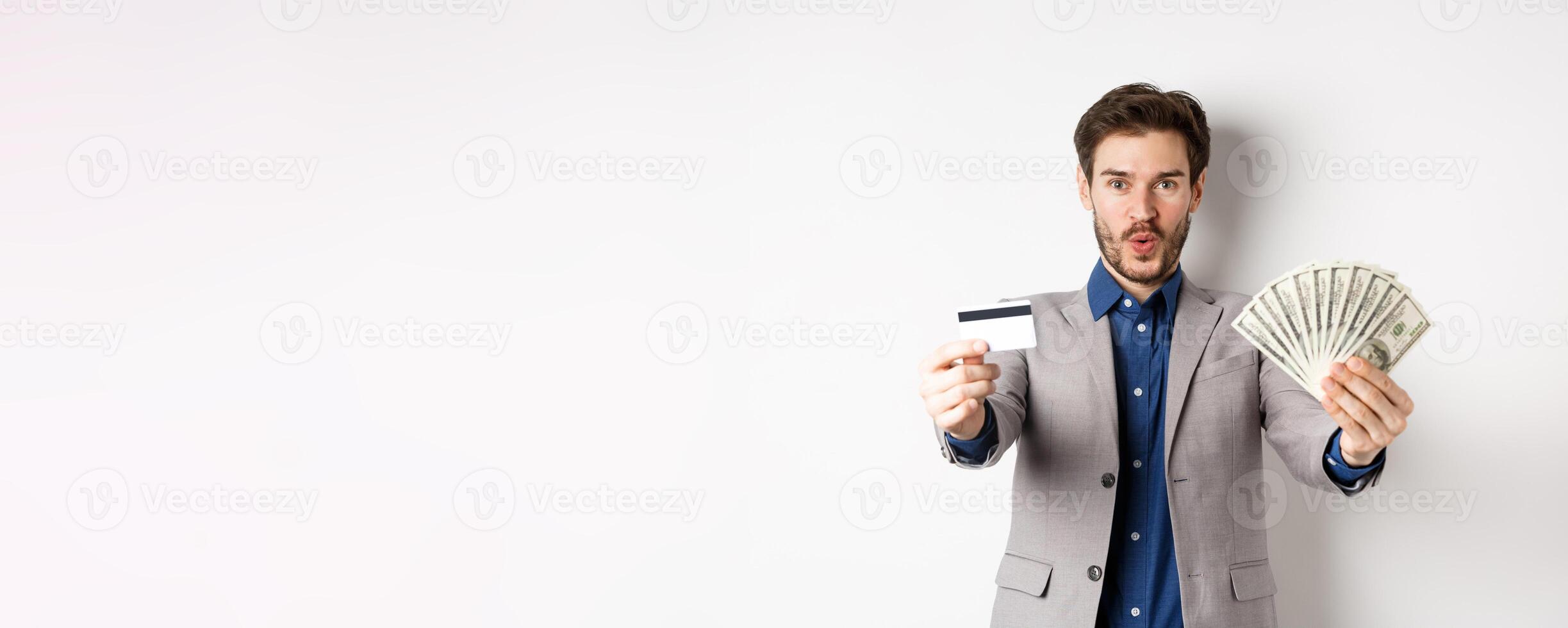 Happy successful businessman in suit showing money and credit card, smiling at camera, white background photo