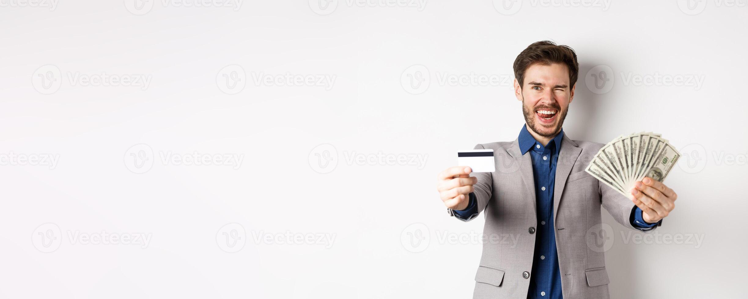 Happy successful businessman in suit showing money and credit card, smiling at camera, white background photo