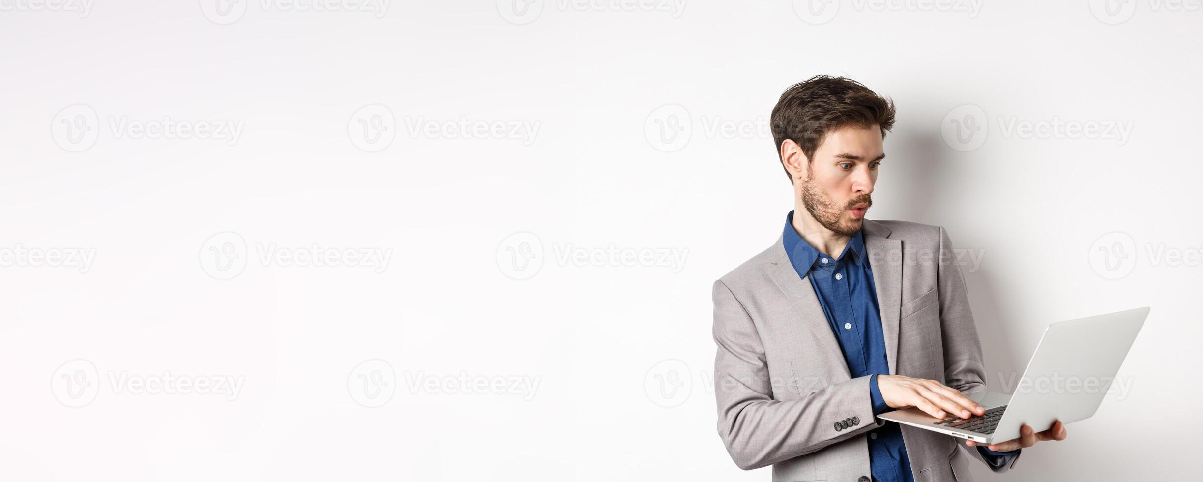 Excited salesman looking at laptop screen amazed, tilt away from excitement, checking out news in network, standing against white background photo