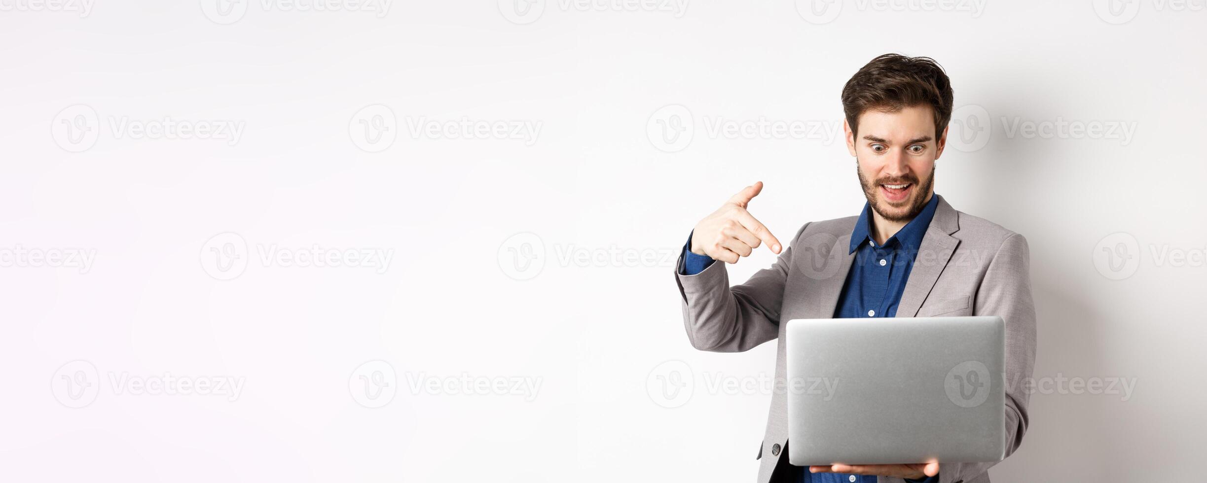 Excited male ceo manager looking and pointing at laptop with amazed smile, checking out special deal online, standing on white background photo