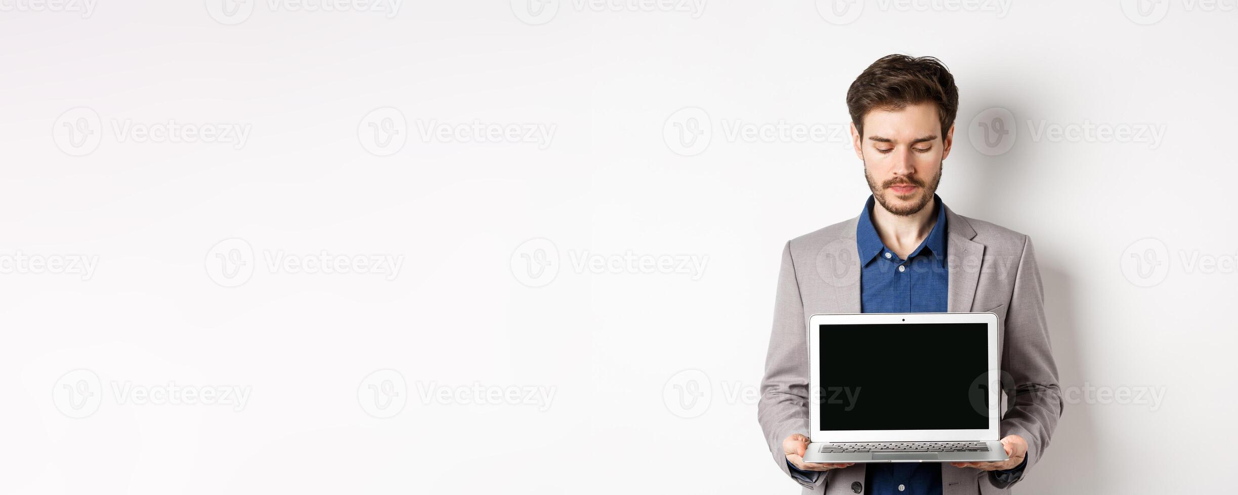 Handsome caucasian businessman in suit showing empty laptop screen, demonstrate promo, standing on white background photo