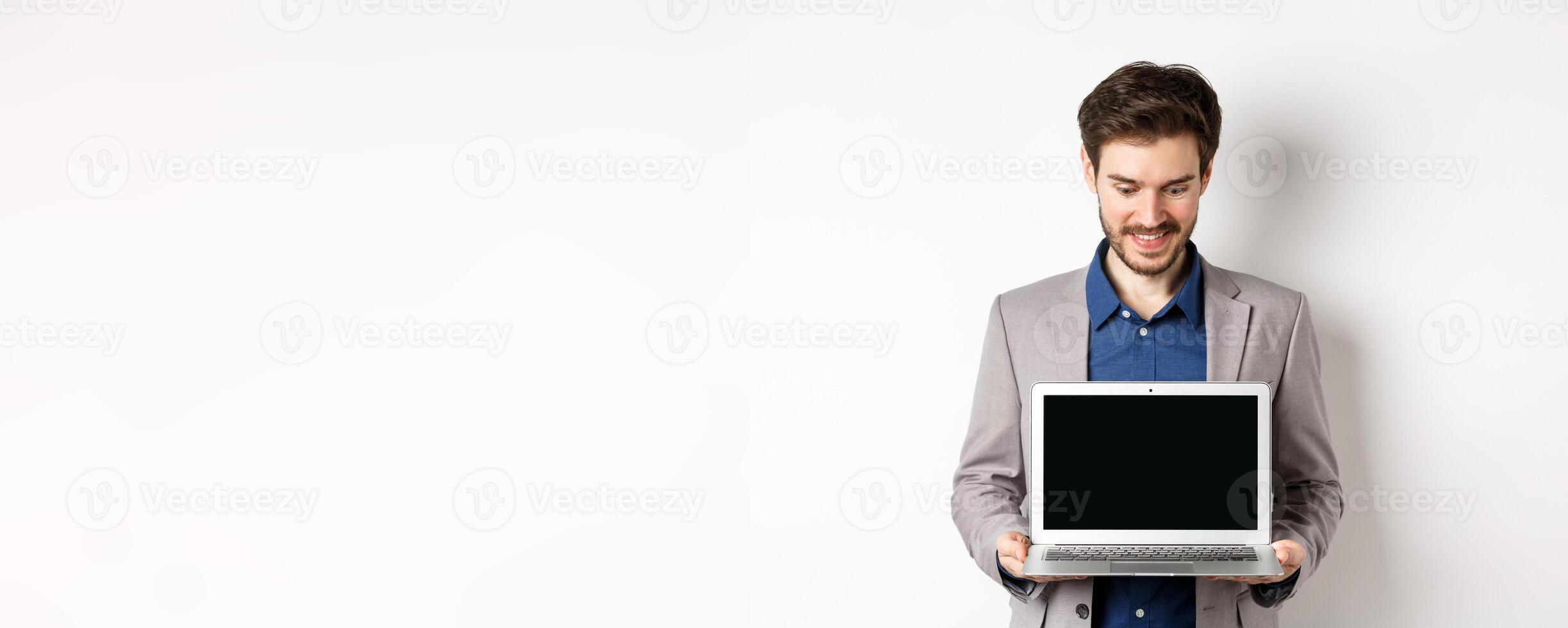 Handsome caucasian businessman in suit showing empty laptop screen, demonstrate promo, standing on white background photo