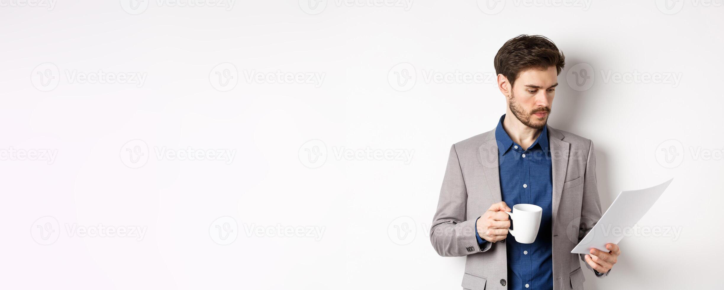 Boss reading documents and drinking morning coffee from mug, looking at paper serious, standing in suit on white background photo