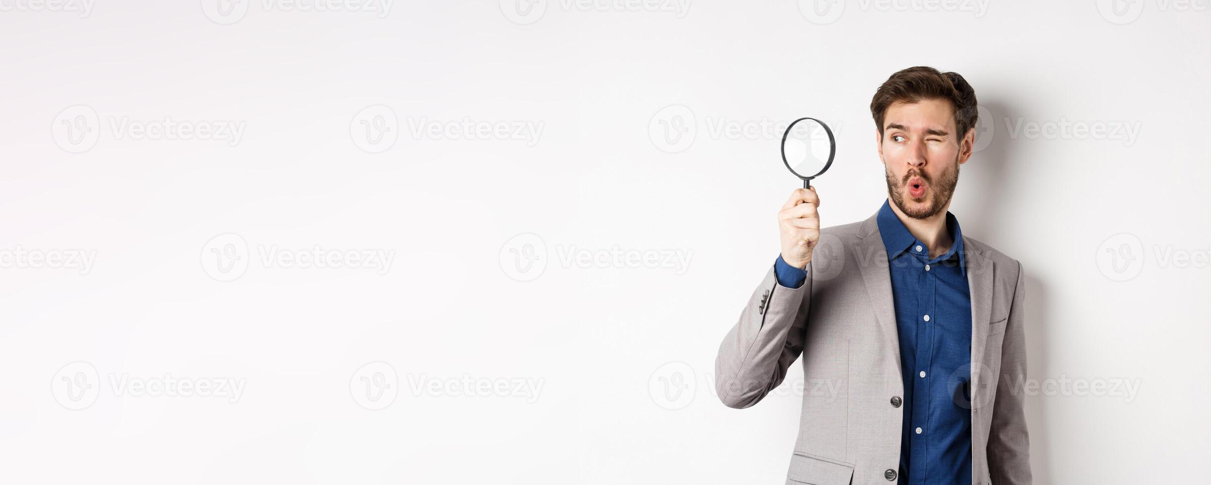 Excited funny guy in suit look through magnifying glass aside, checking out awesome thing, found something, white background photo