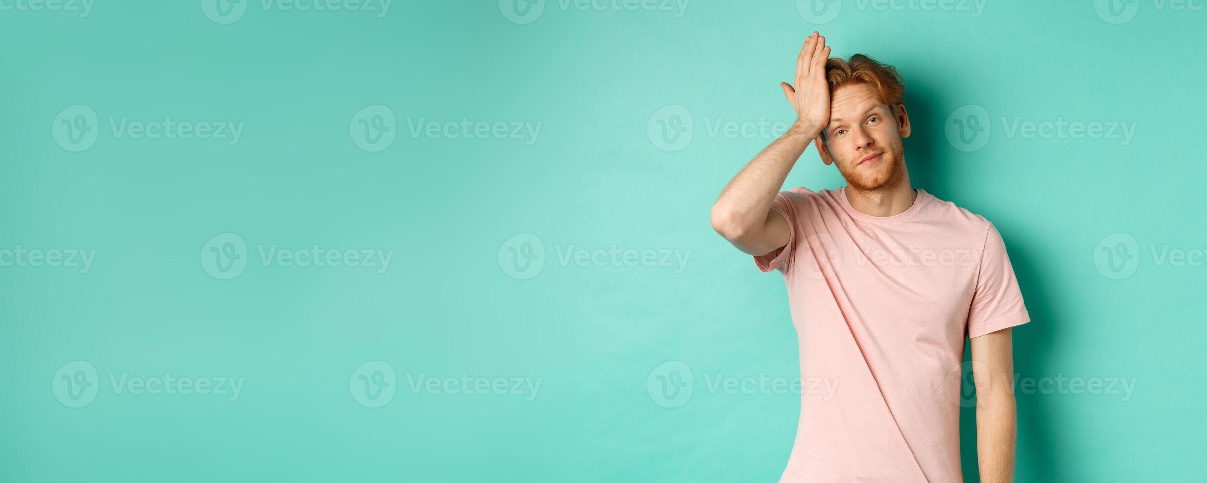 Annoyed and bothered redhead male model showing facepalm gesture, standing over mint background photo