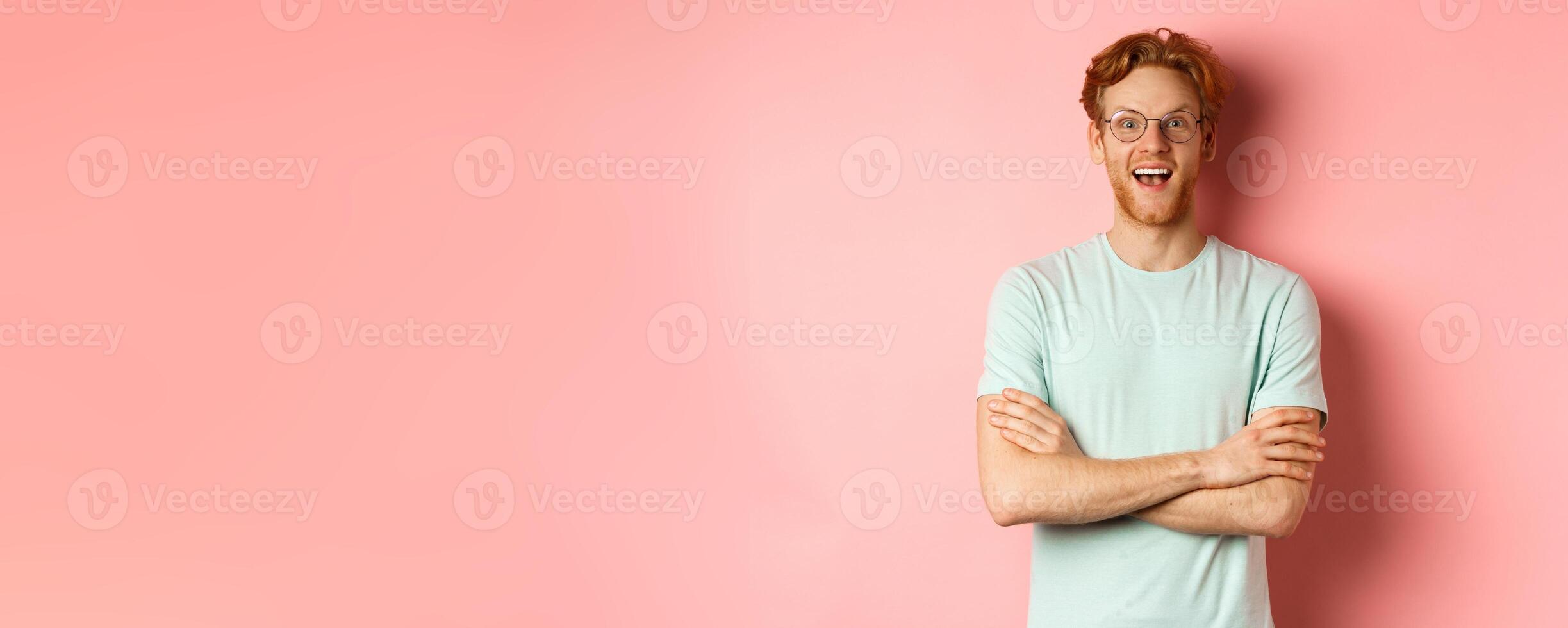Portrait of cheerful european man in glasses looking amazed at camera, see interesting promotion, standing amused over pink background photo