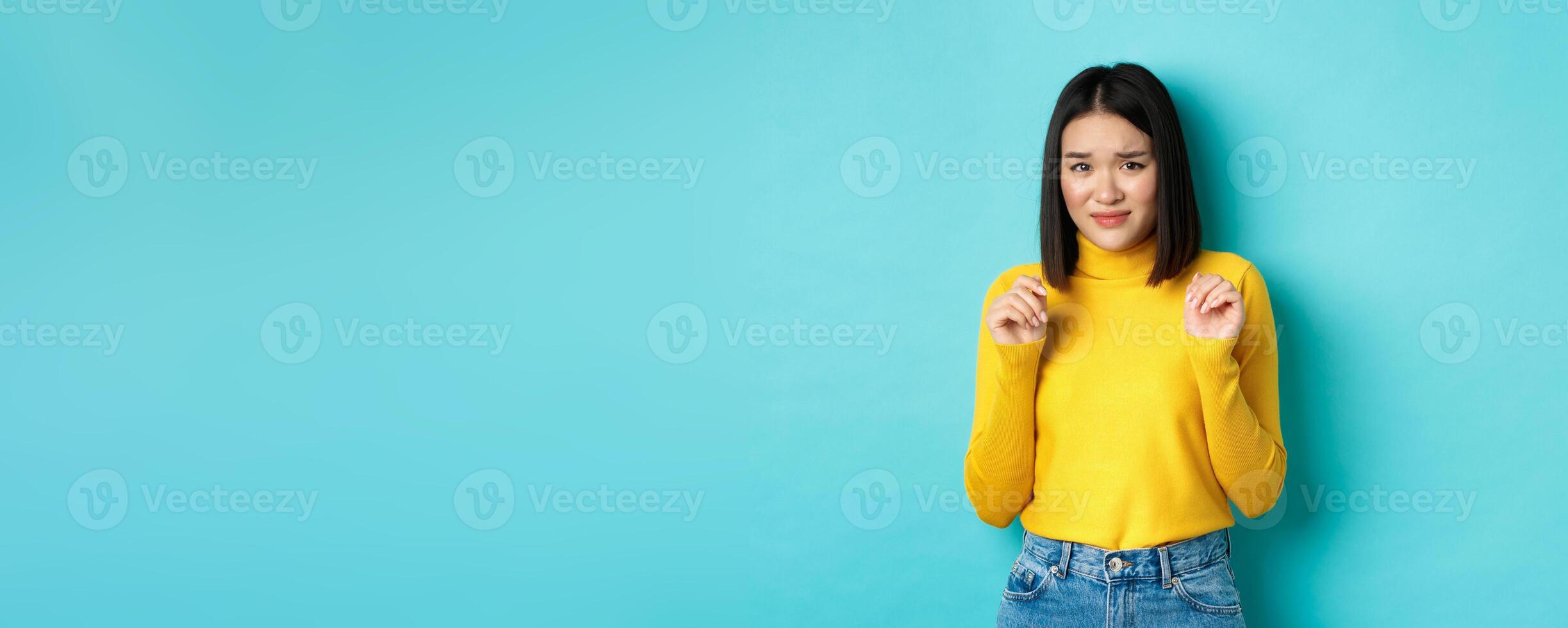 Image of disgusted chinese woman looking with cringe and aversion, grimacing and step backwards from something disgusting, standing over blue background photo