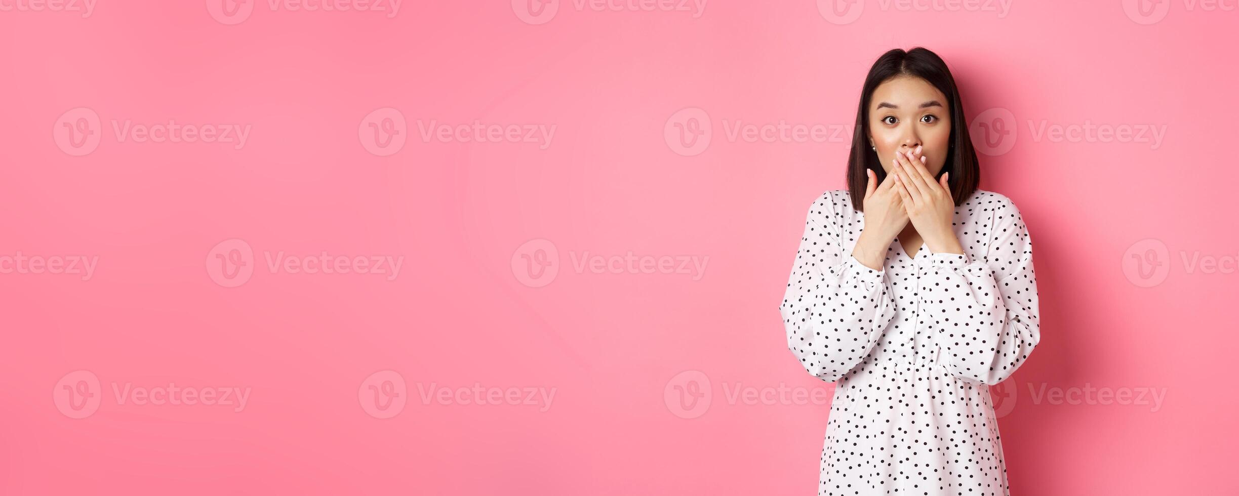 Image of surprised asian female model gasping, cover mouth and looking at camera, standing amazed against pink background photo