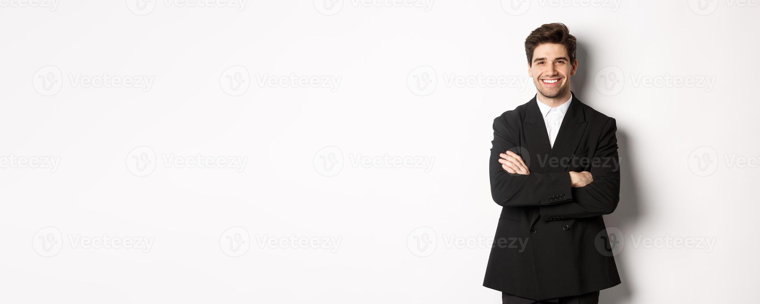 Handsome and confident bearded man, standing in formal suit with hands crossed on chest, smiling satisfied, attend party or work event, standing over white background photo