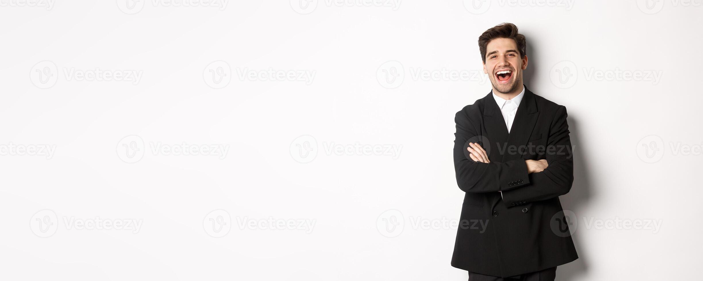 Portrait of attractive adult man in suit laughing and looking happy, standing in suit with hands crossed over chest, posing against white background photo