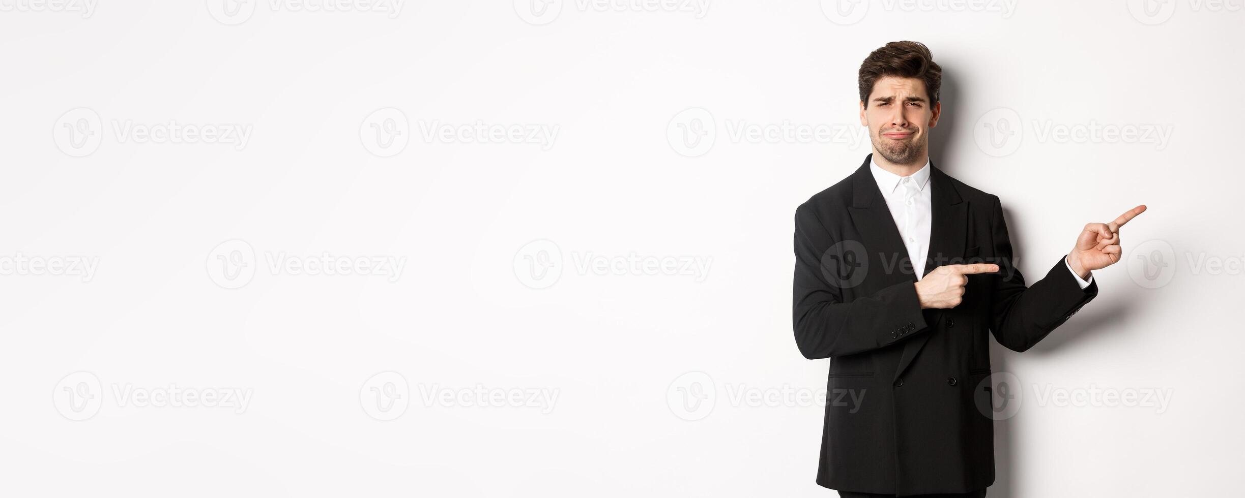 Image of devestated man in party suit, crying and complaining, pointing fingers right at something disappointing, standing over white background photo