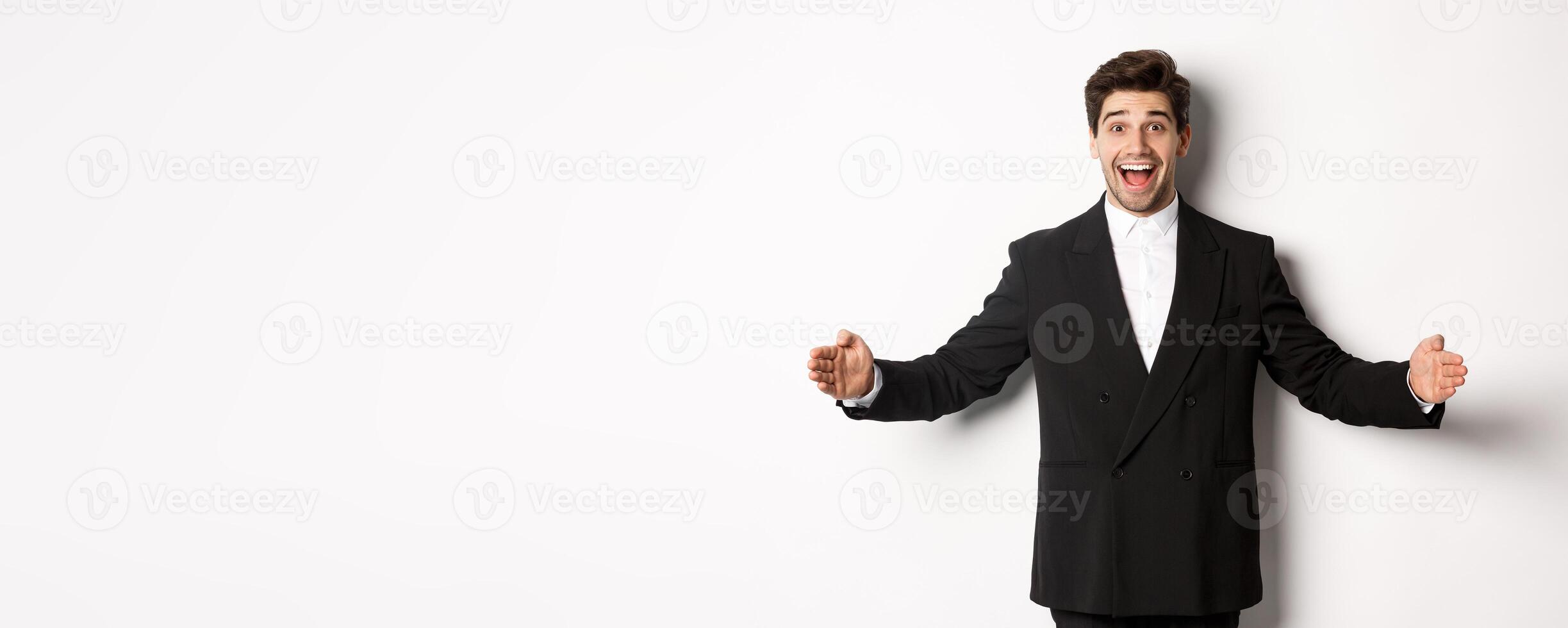 Portrait of excited handsome man in suit, shaping big object on copy space and smiling amazed, holding something, standing over white background photo