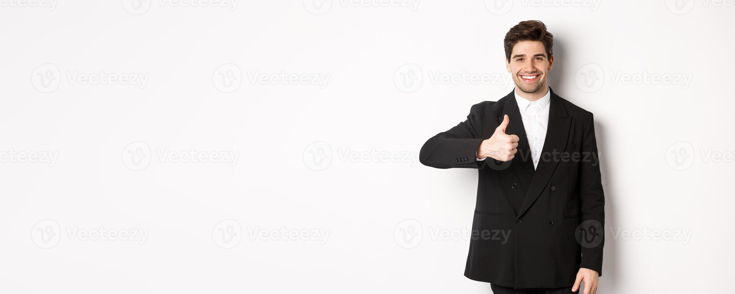 Portrait of handsome and confident male realtor, showing thumb-up and smiling, guarantee quality and recommending company, standing over white background photo