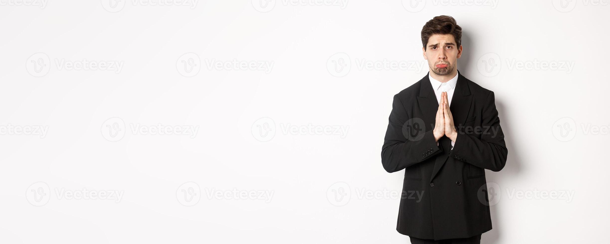 Miserable clingy guy need help, pouting silly and begging for something, asking for favour, standing against white background in black suit photo