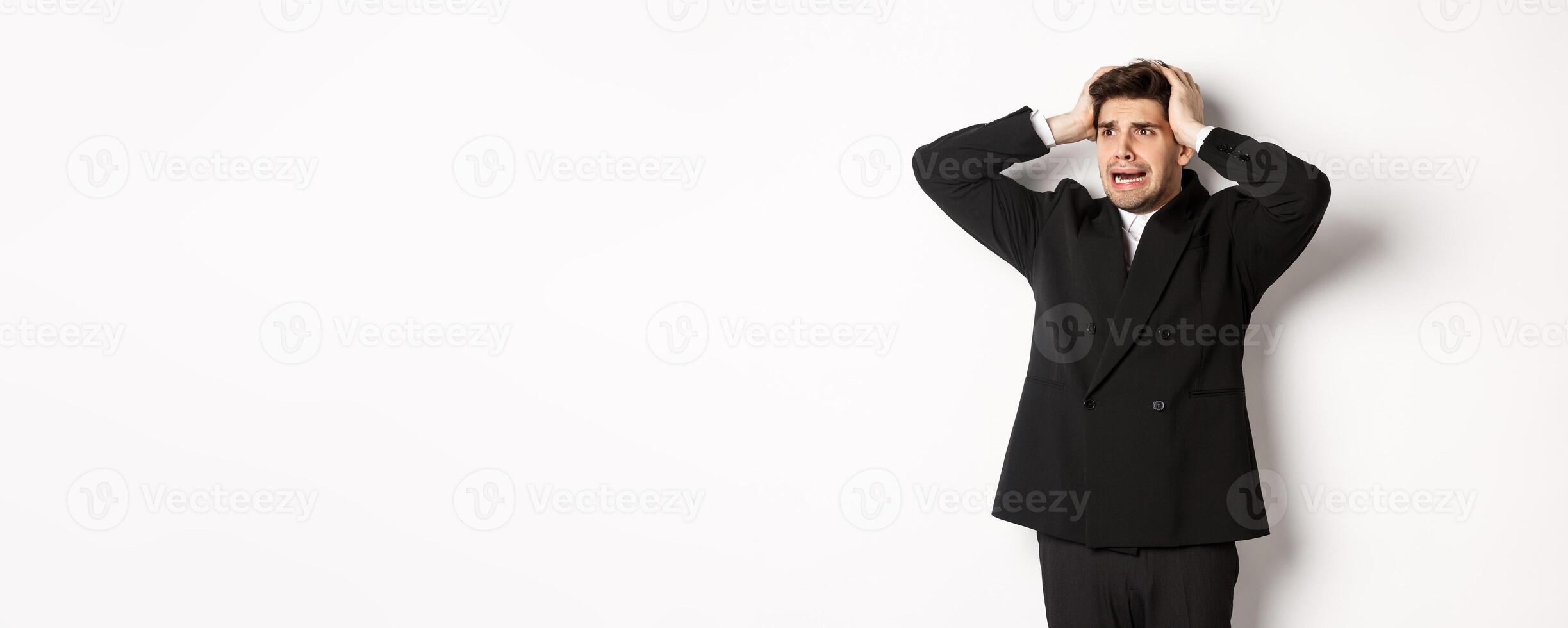 Image of anxious businessman start to panic, looking left with worried expression, standing in black suit over white background photo