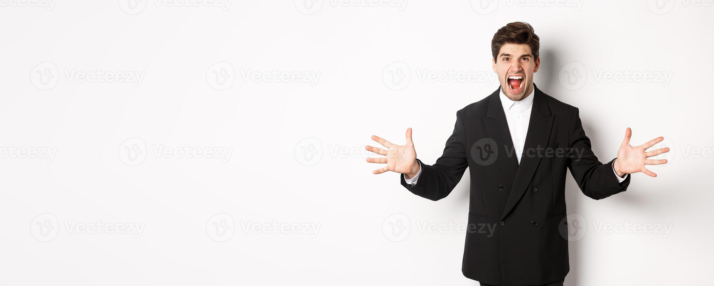 Portrait of pissed-off and frustrated businessman in suit, shouting angry and shaking hands, standing distressed against white background photo