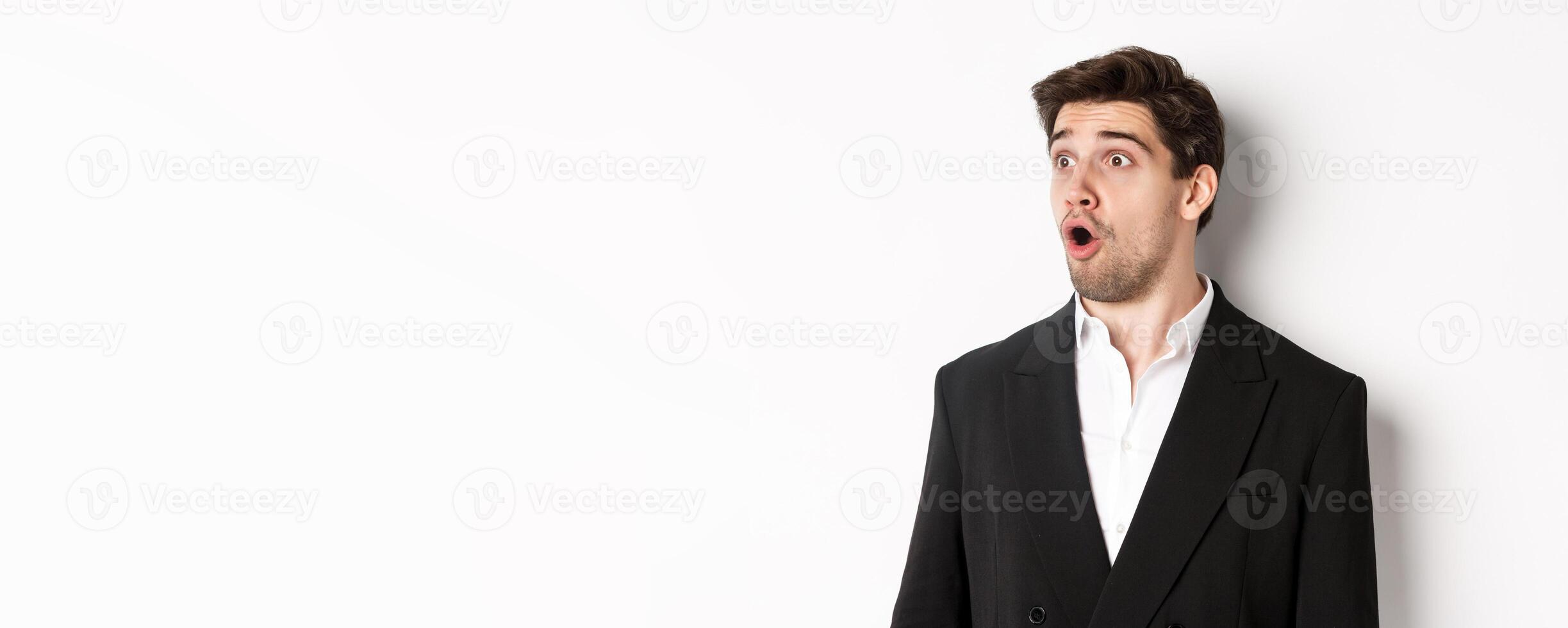 Close-up of impressed guy in trendy suit, open mouth and looking left wondered, standing against white background photo