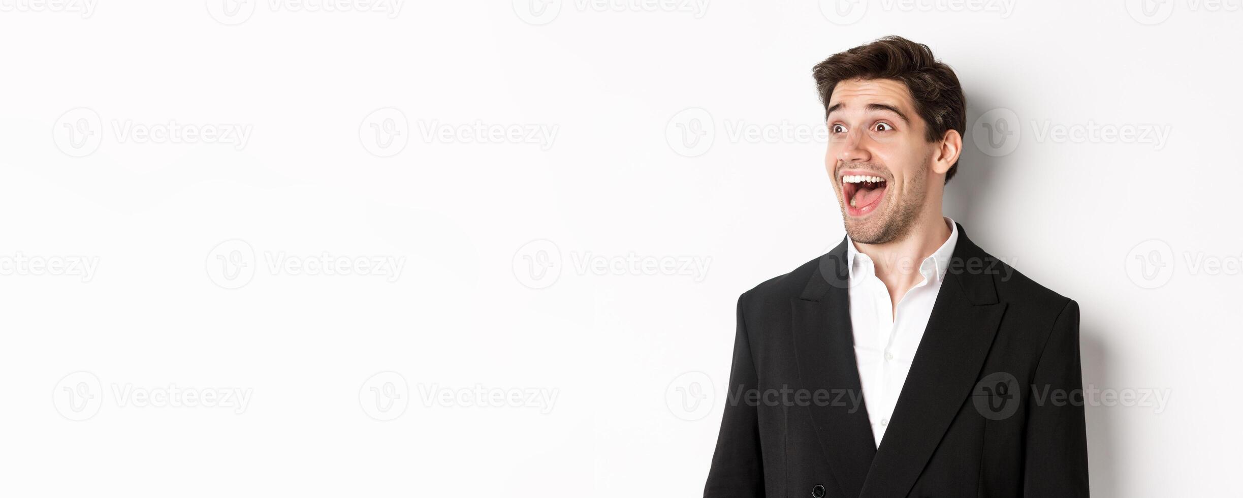 Close-up of handsome male entrepreneur in suit, looking left and smiling amazed, standing against white background photo