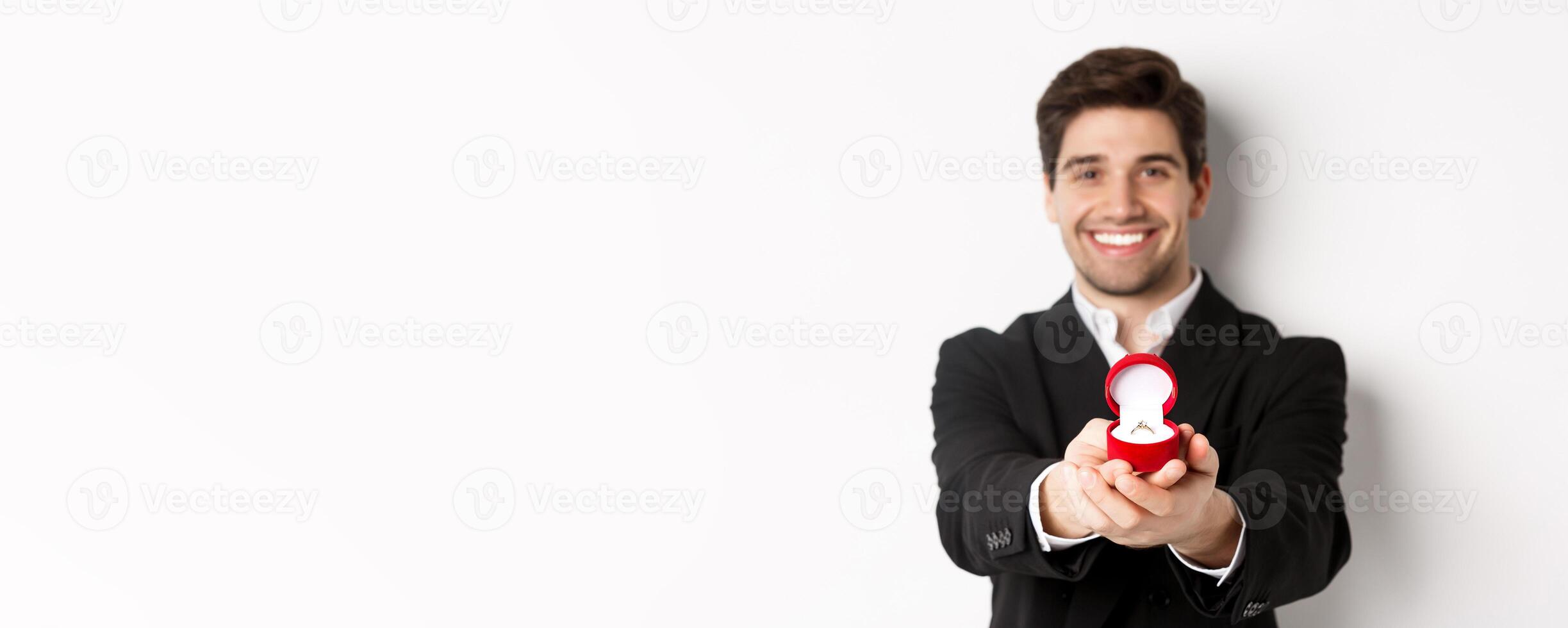 Image of handsome man looking romantic, giving you an engagement ring, making proposal to marry him, standing against white background photo
