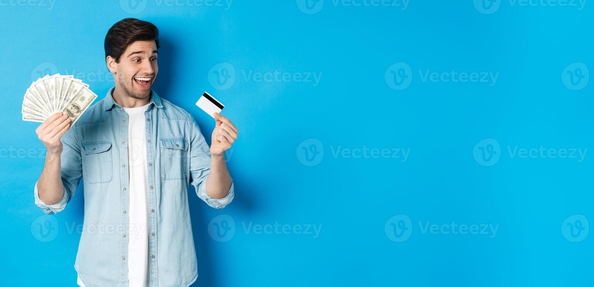 Surprised and happy man looking at credit card and showing money, concept of bank loan, finance and income. photo