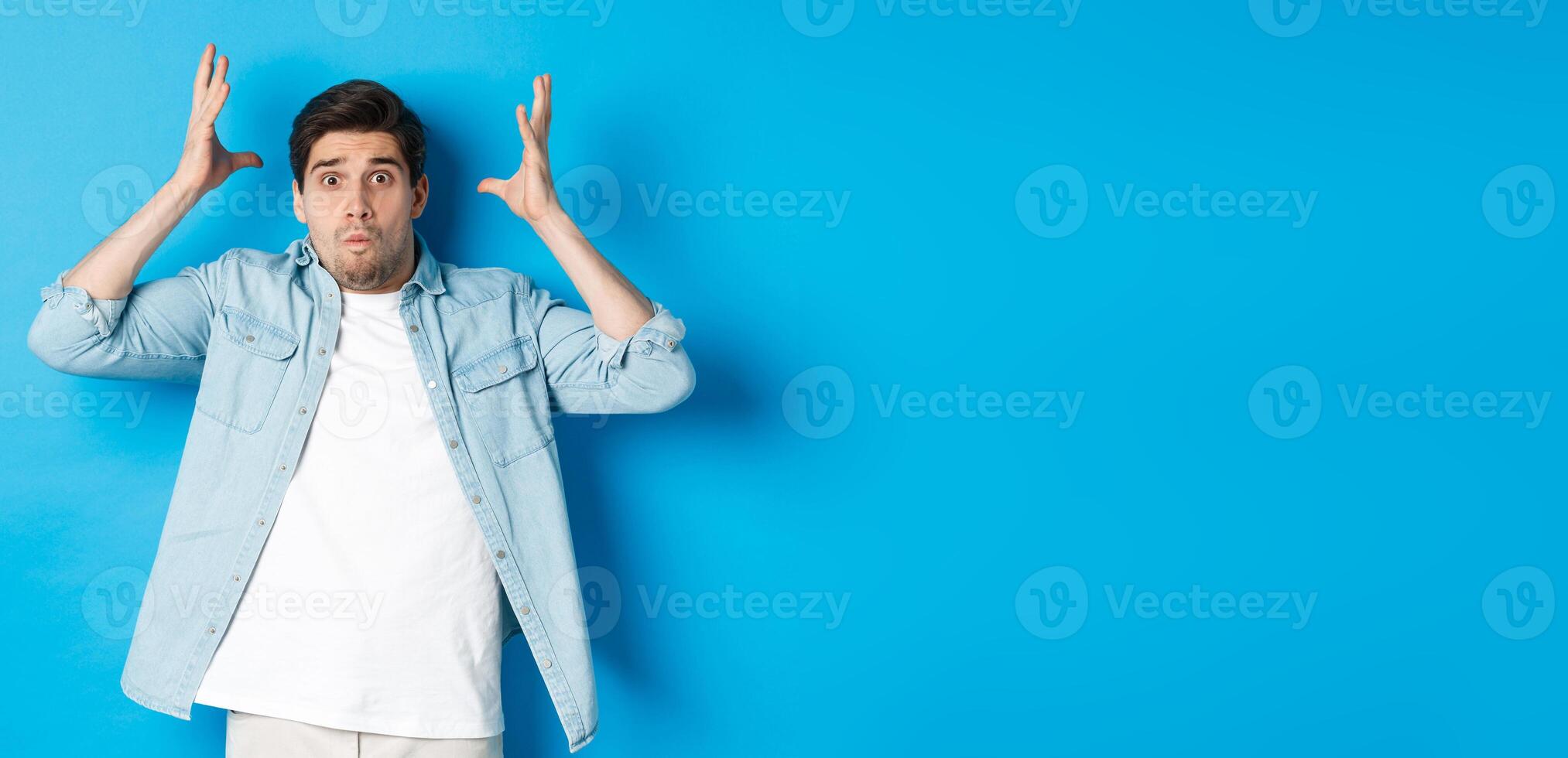 Distressed guy showing mind blowing gesture, looking frustrated and anxious, standing against blue background photo