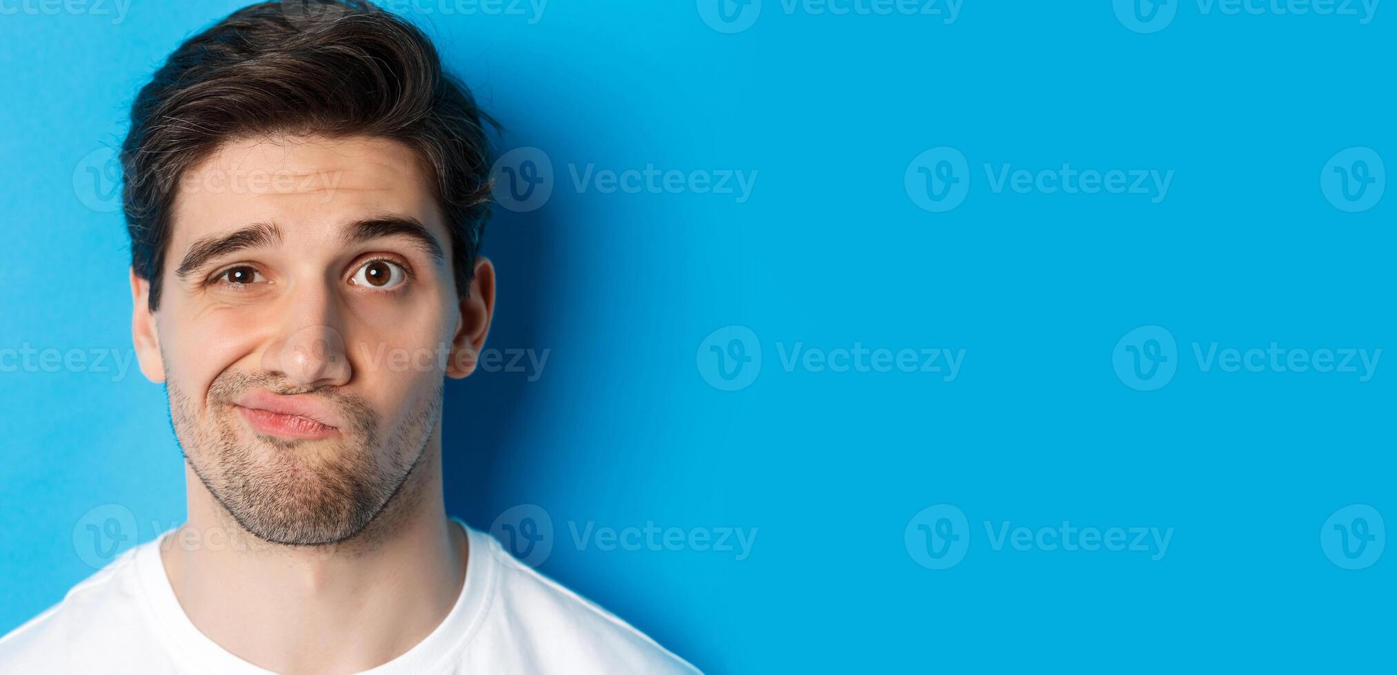 Headshot of skeptical guy looking at something unamusing, grimacing and standing reluctant against blue background photo