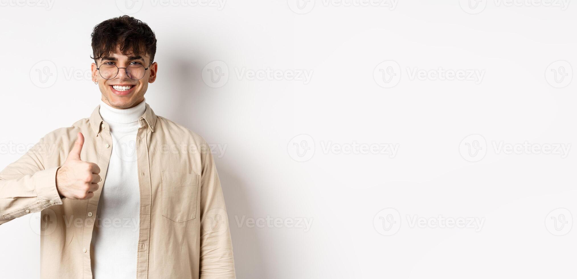 Positive smiling man showing thumbs up and looking satisfied, recommending and approving thing, standing pleased on white background photo