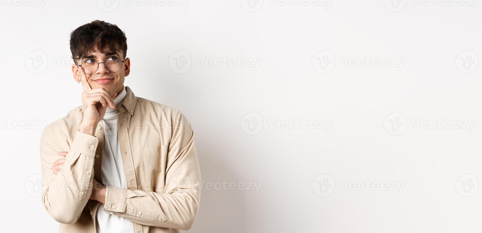 Image of happy dreamy young man imaging something good, smiling and looking at upper right corner thoughtful, standing on white background photo