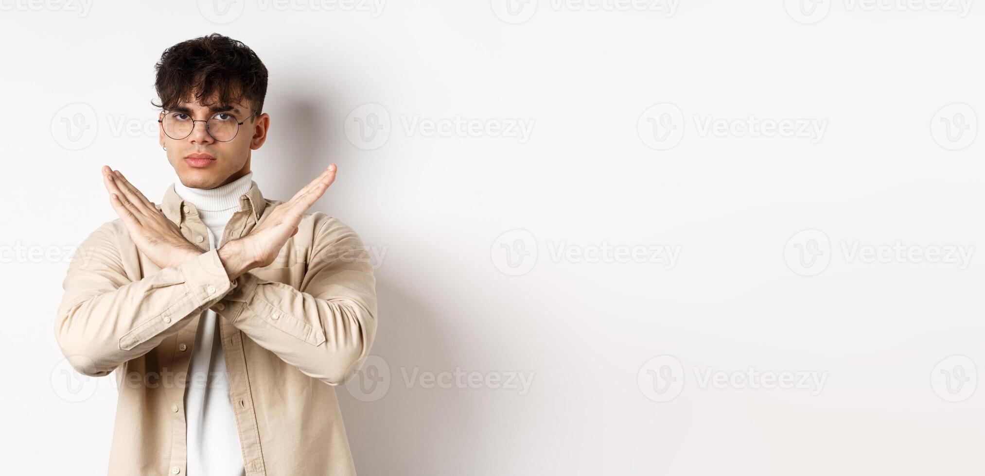 Image of serious young guy in glasses say no, showing cross gesture, make stop sign to disagree or prohibit something, standing on white background photo