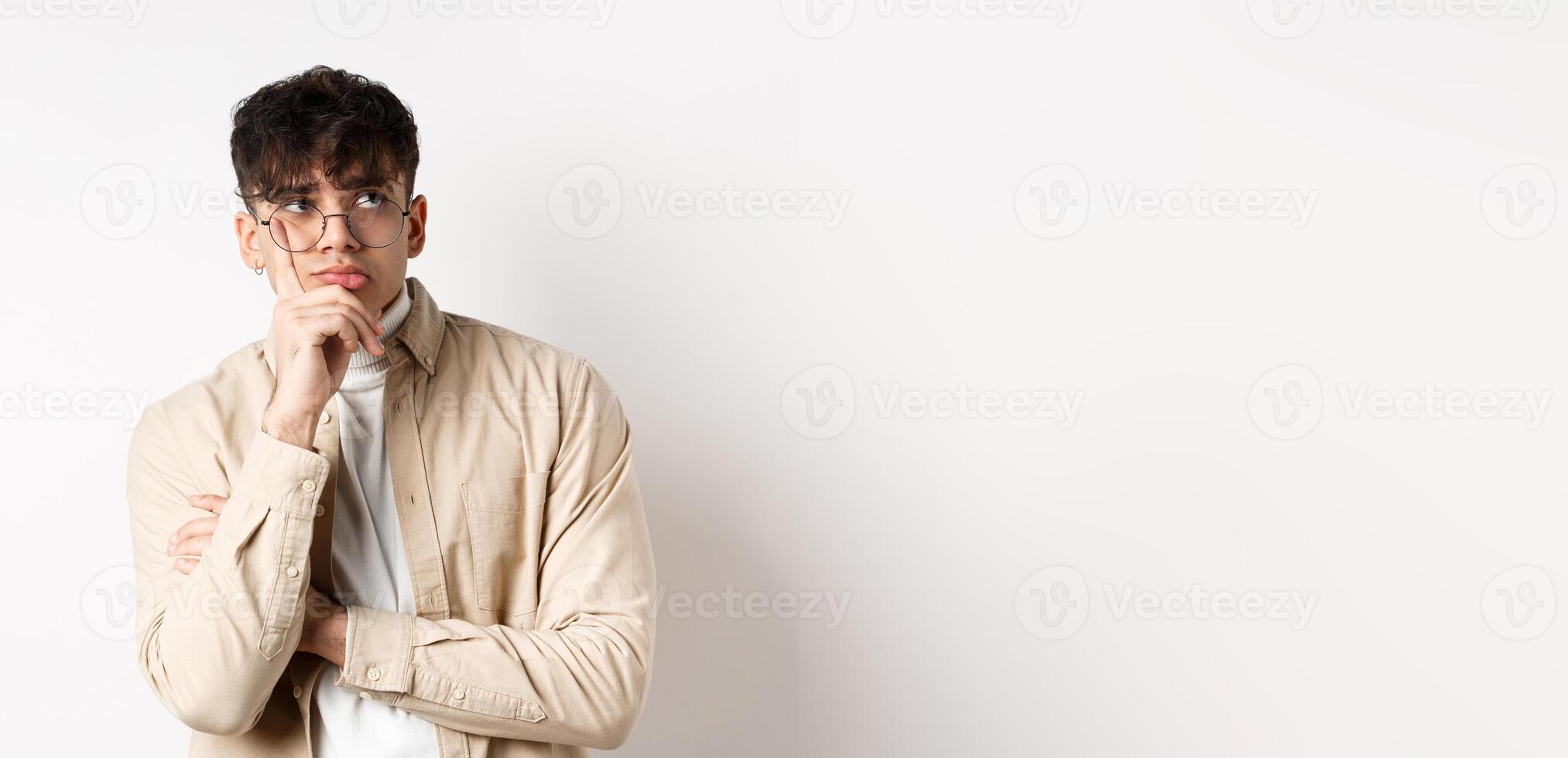 Sad and lonely young man looking at empty space with distressed face, standing thoughtful on white background photo