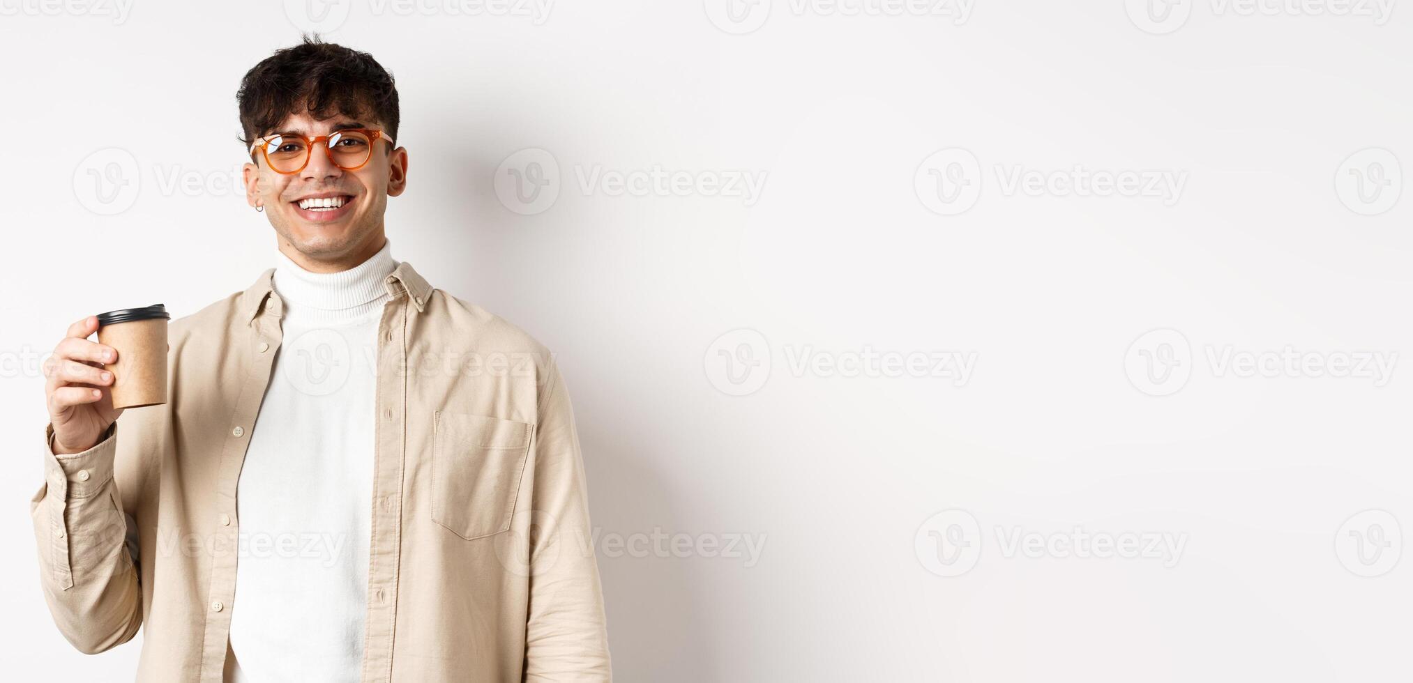 Real people. Happy young man drinking coffee from paper cup, order takeaway at favourite cafe, smiling and looking pleased at camera, white background photo