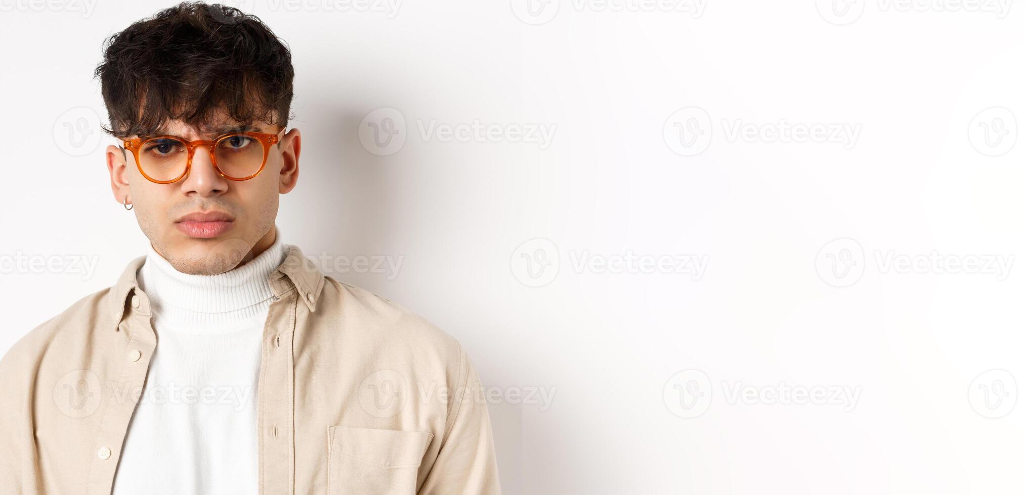 Close up portrait of angry frowning guy looking with despise, standing mad on white background, wearing glasses photo