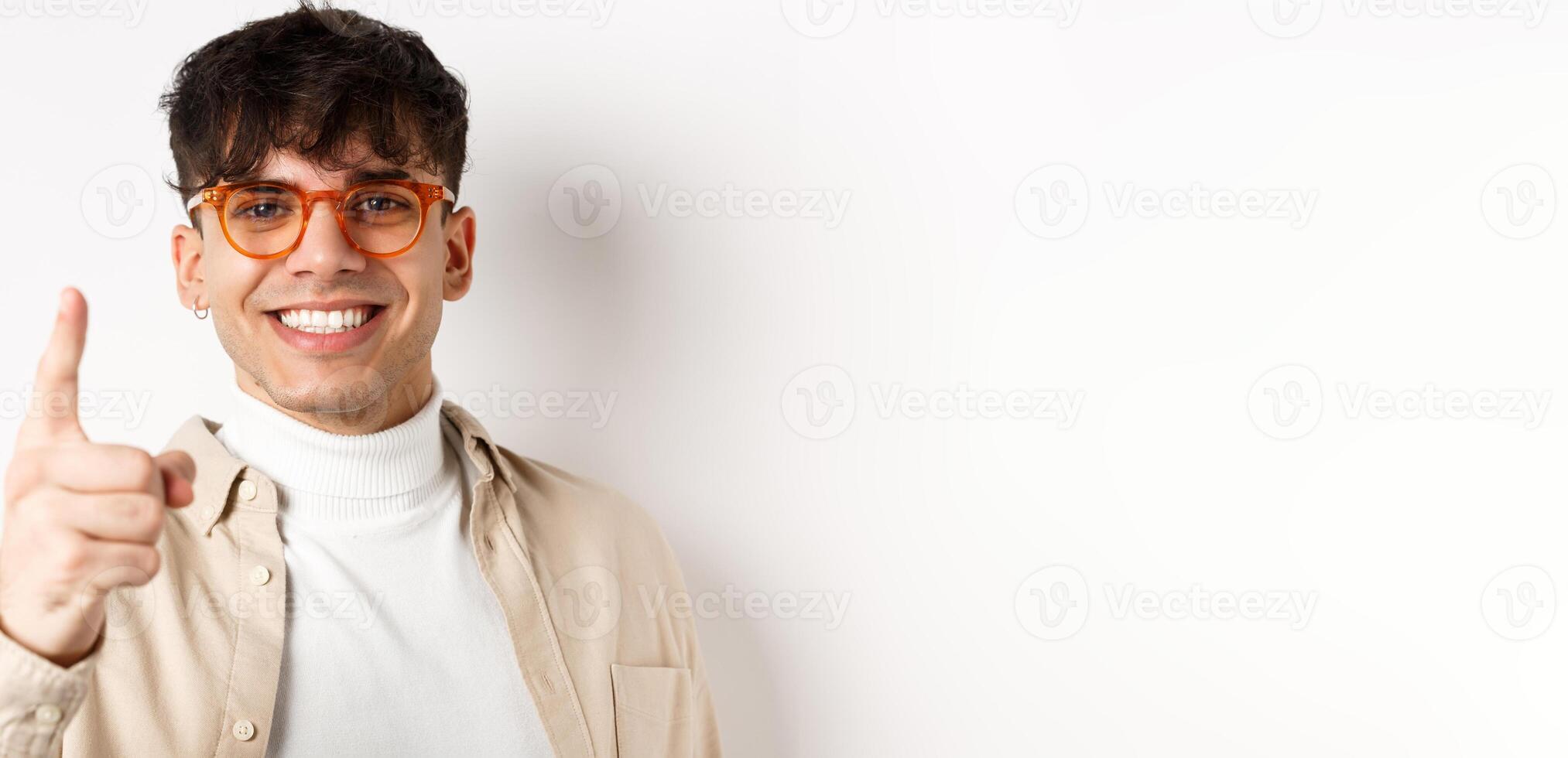 Close-up of lucky handsome man in glasses, smiling and pointing finger at camera, praising something good, standing on white background photo