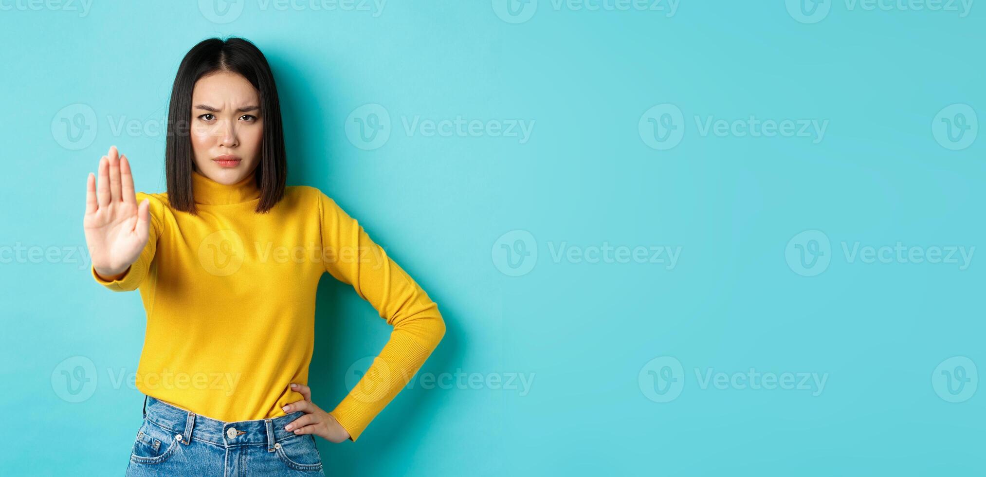 Confident and serious asian woman tell no, showing stop gesture to prohibit and warn, disagree with someone, standing upset against blue background photo