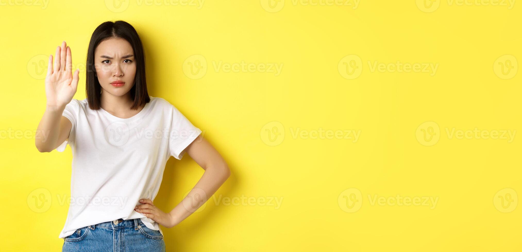 Confident and serious asian woman tell no, showing stop gesture to prohibit and warn, disagree with someone, standing upset against yellow background photo
