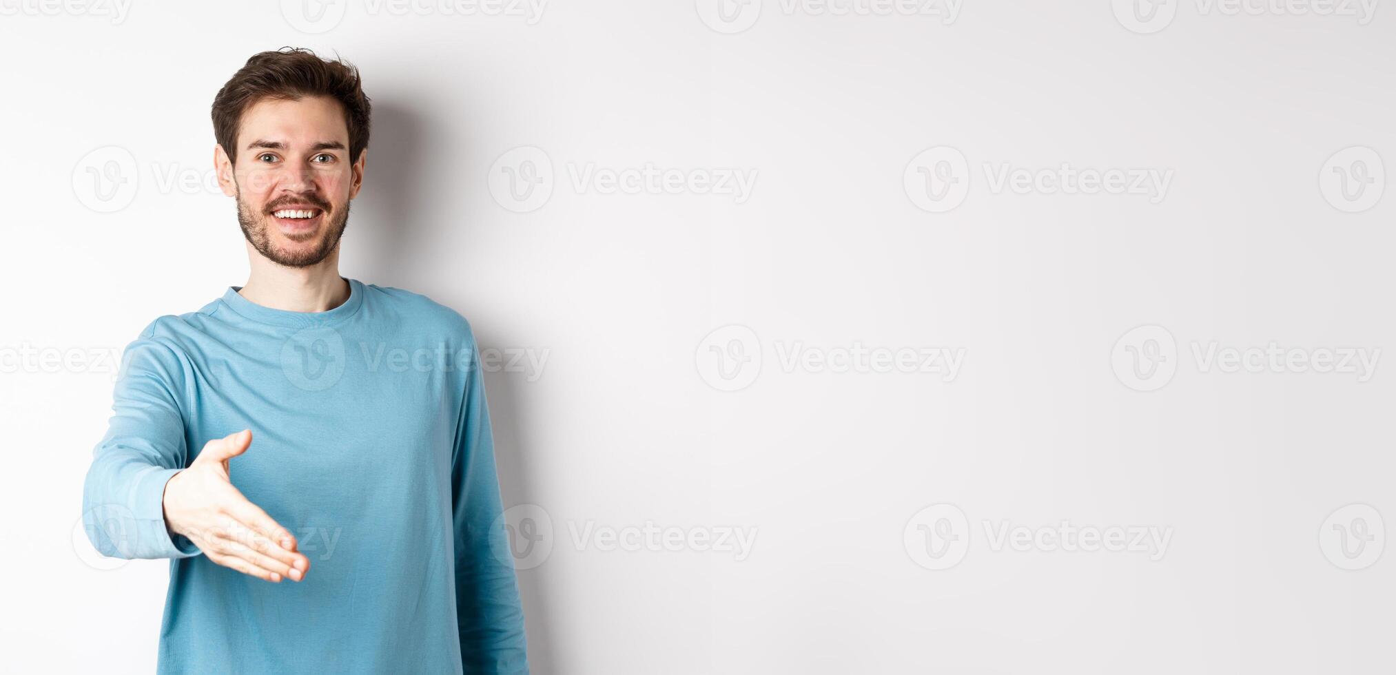 Friendly smiling man stretch out hand, saying hello and give arm for handshake, standing over white background photo